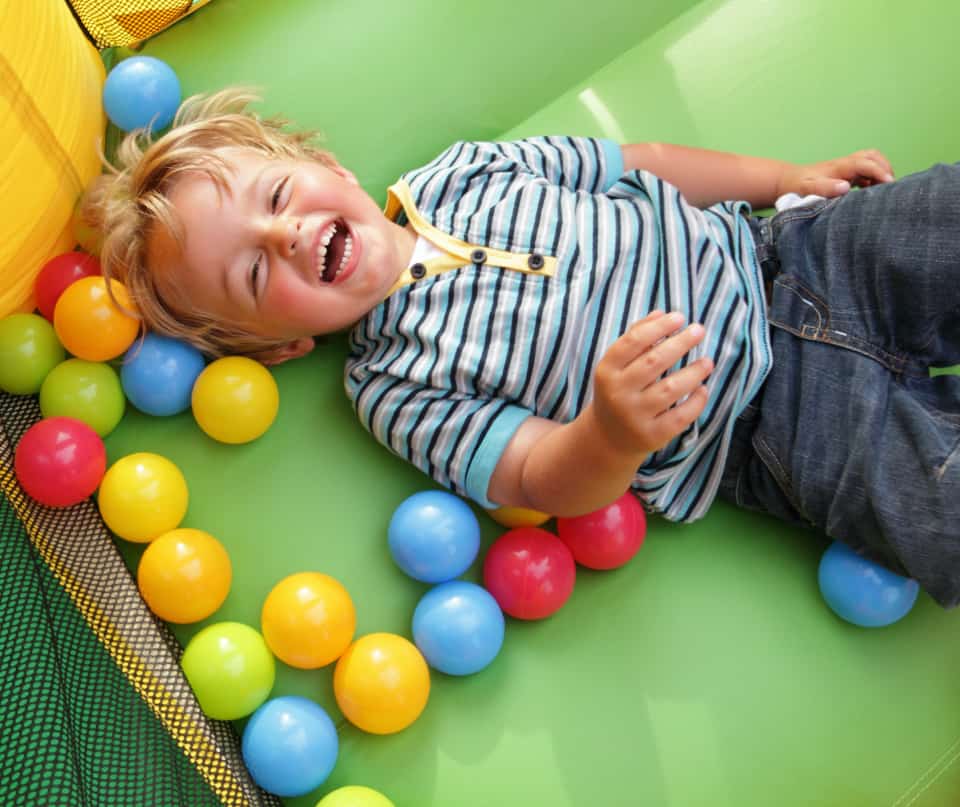 child playing in bounce house with colorful balls at kids party